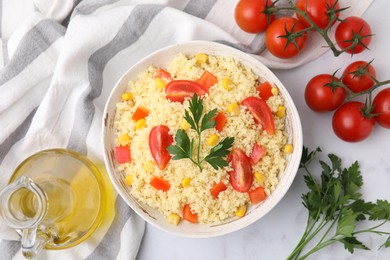 Tasty couscous with parsley, corn and tomatoes served on white table, flat lay