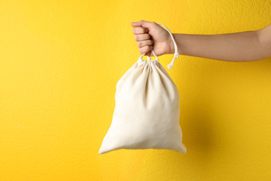 Woman holding full cotton eco bag on yellow background, closeup