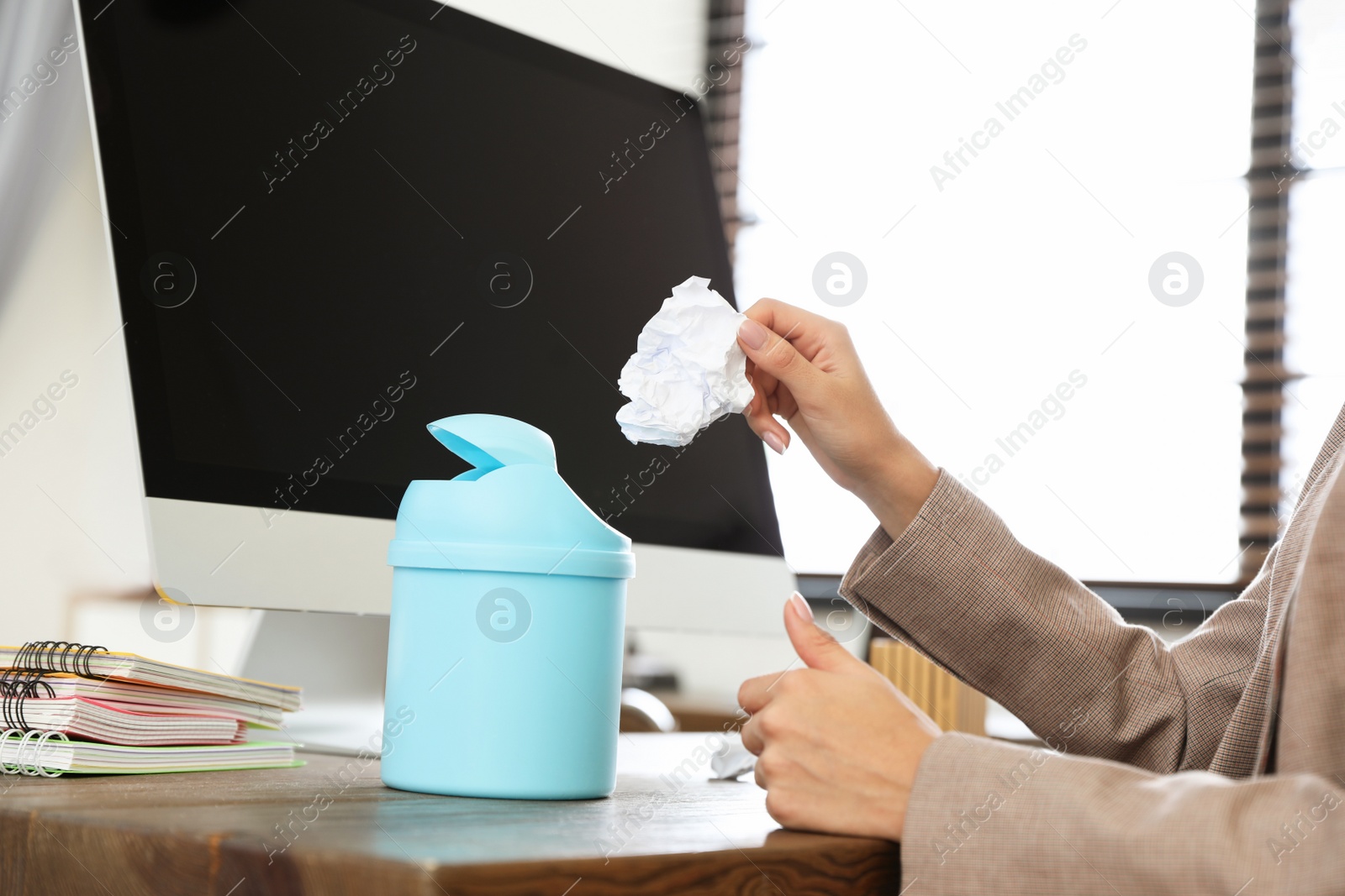 Photo of Young woman throwing paper into recycling bin at office, closeup