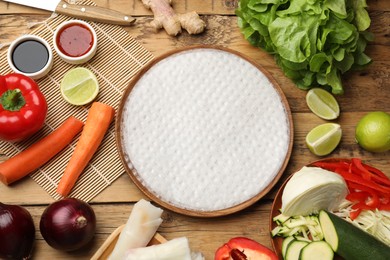 Making delicious spring rolls. Rice paper and other ingredients on wooden table, flat lay