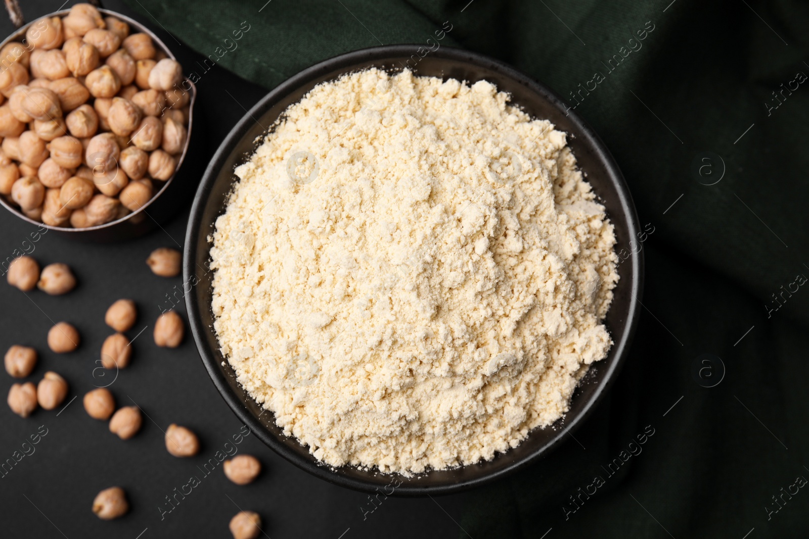 Photo of Chickpea flour in bowl and seeds on black table, flat lay