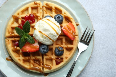 Delicious Belgian waffles with ice cream, berries and caramel sauce served on grey table, top view