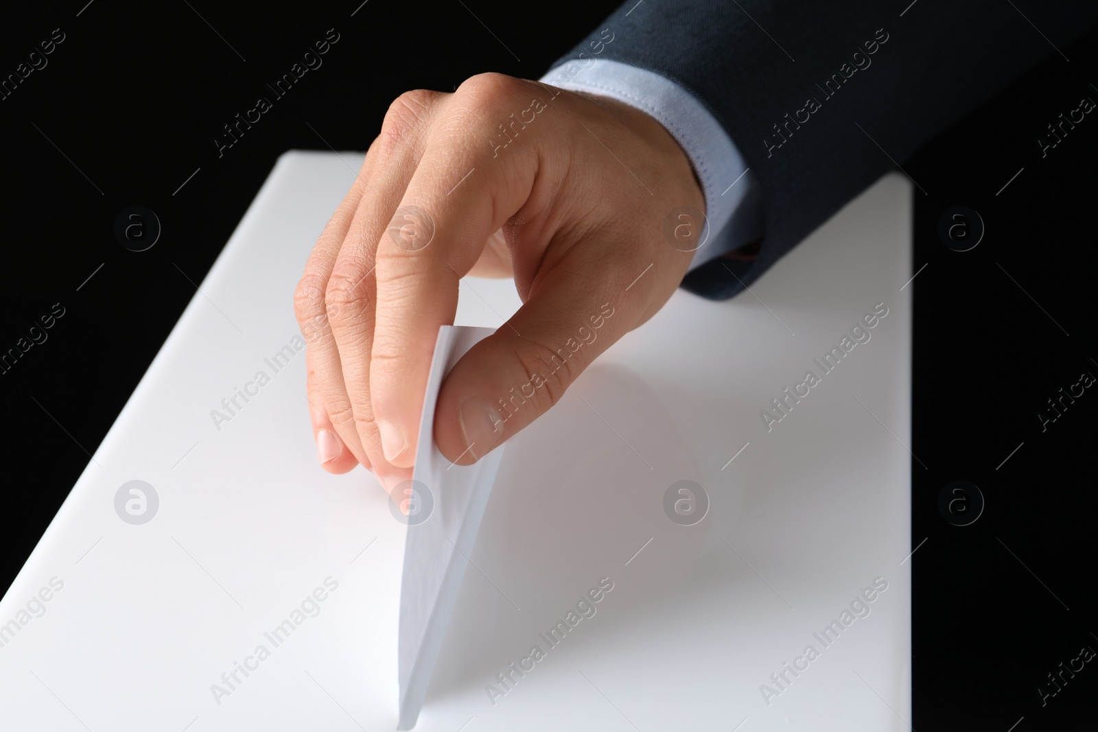 Photo of Man putting his vote into ballot box on black background, closeup