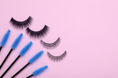 Photo of Fake eyelashes and brushes on pink background, flat lay. Space for text