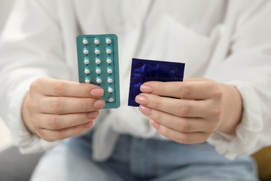 Woman holding condom and contraceptive pills, closeup. Choosing birth control method