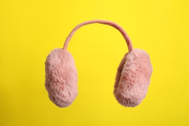 Photo of Fluffy earmuffs on yellow background. Stylish winter accessory
