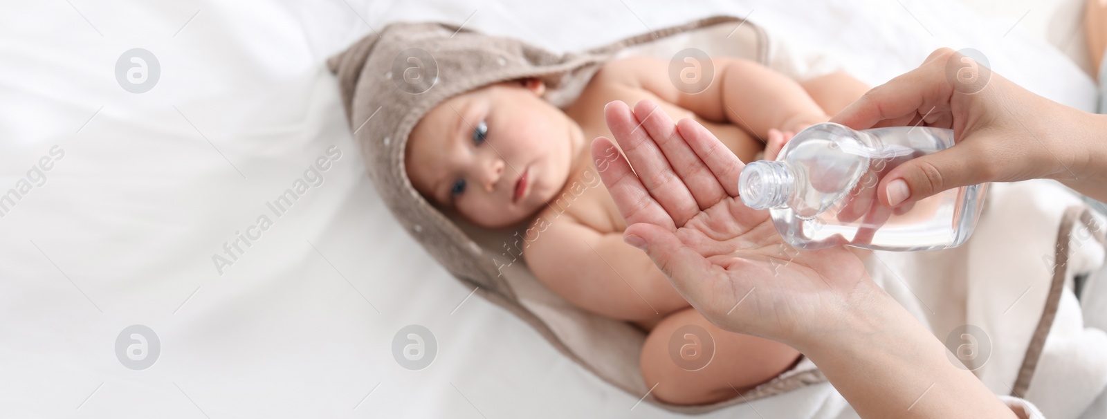 Image of Mother with bottle of massage oil near baby on bed, closeup. Banner design with space for text