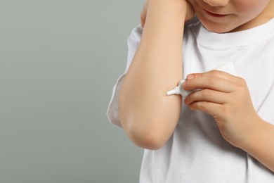 Child applying ointment onto elbow against grey background, closeup. Space for text