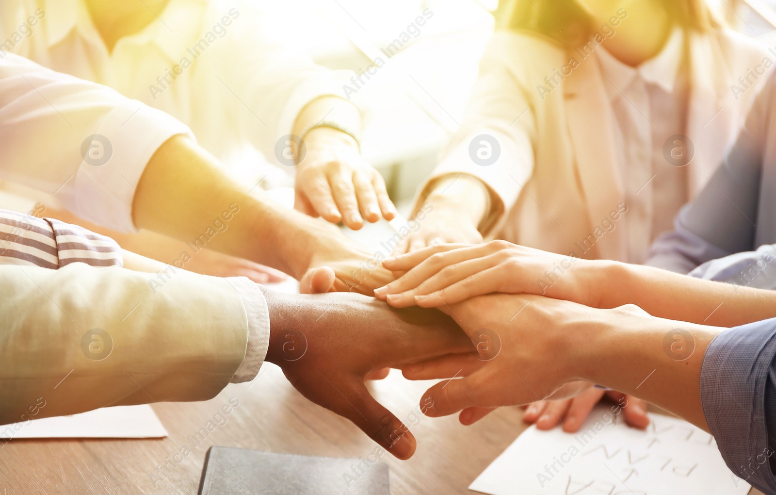 Image of Volunteers putting hands together at table in sunlit room, closeup 