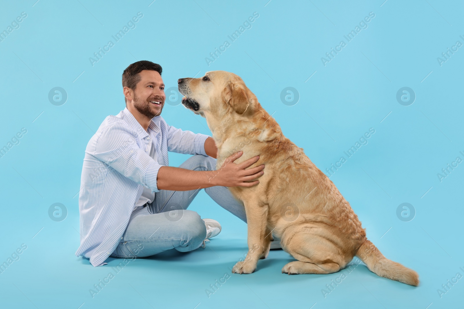 Photo of Man with adorable Labrador Retriever dog on light blue background. Lovely pet