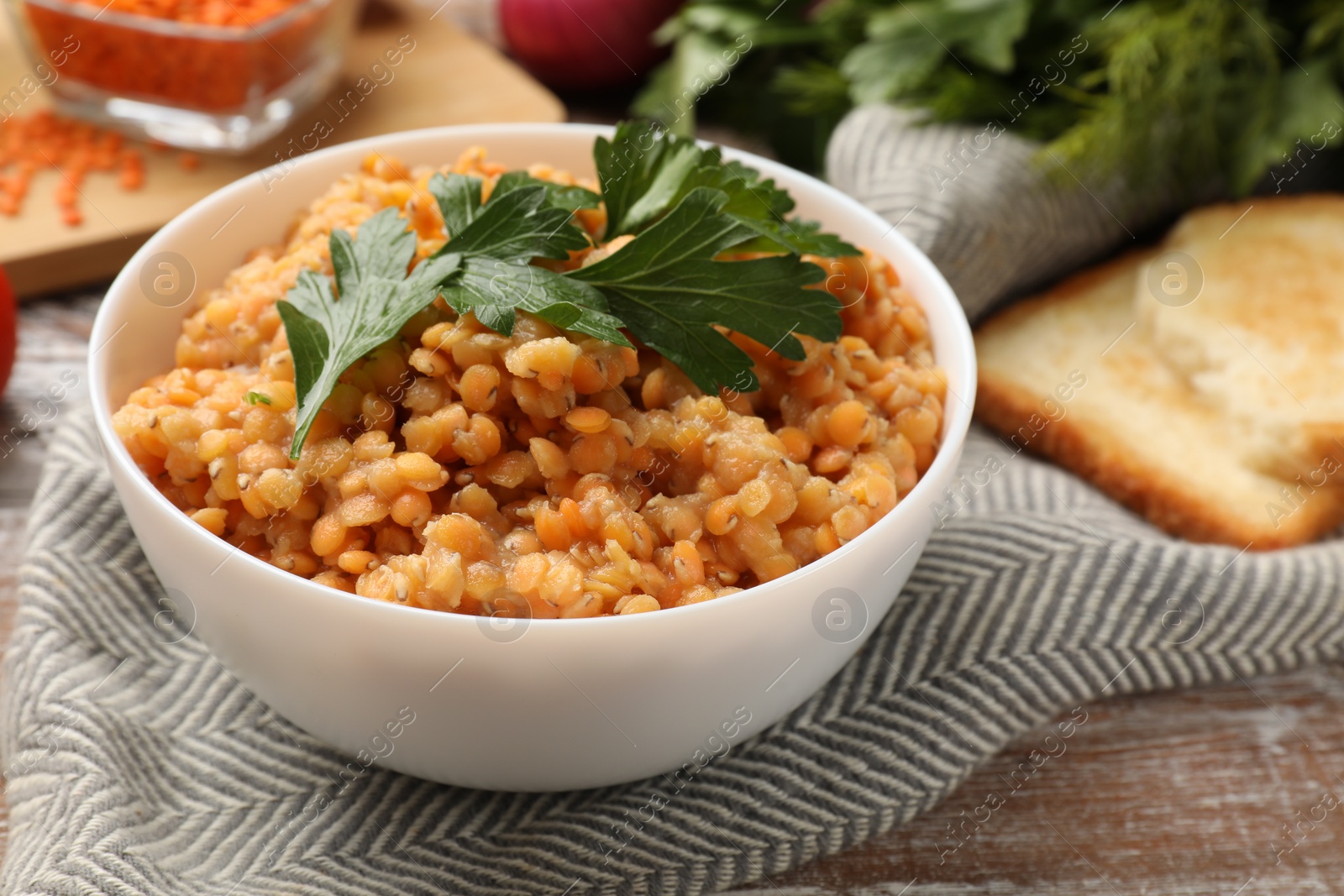 Photo of Delicious red lentils with parsley in bowl on wooden table, closeup