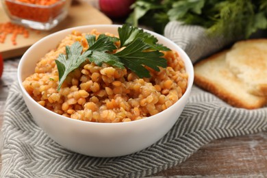 Delicious red lentils with parsley in bowl on wooden table, closeup