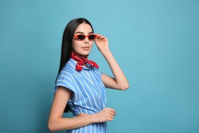 Photo of Fashionable young woman in stylish outfit with bandana on light blue background, space for text