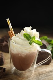 Photo of Glass cup of delicious hot chocolate with whipped cream and mint on wooden table