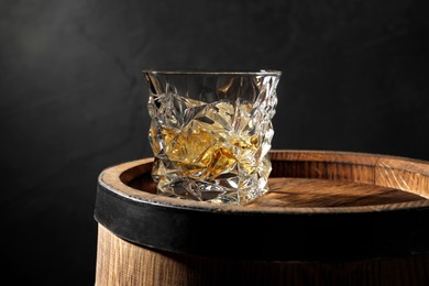 Glass of whiskey on wooden barrel against black background, closeup