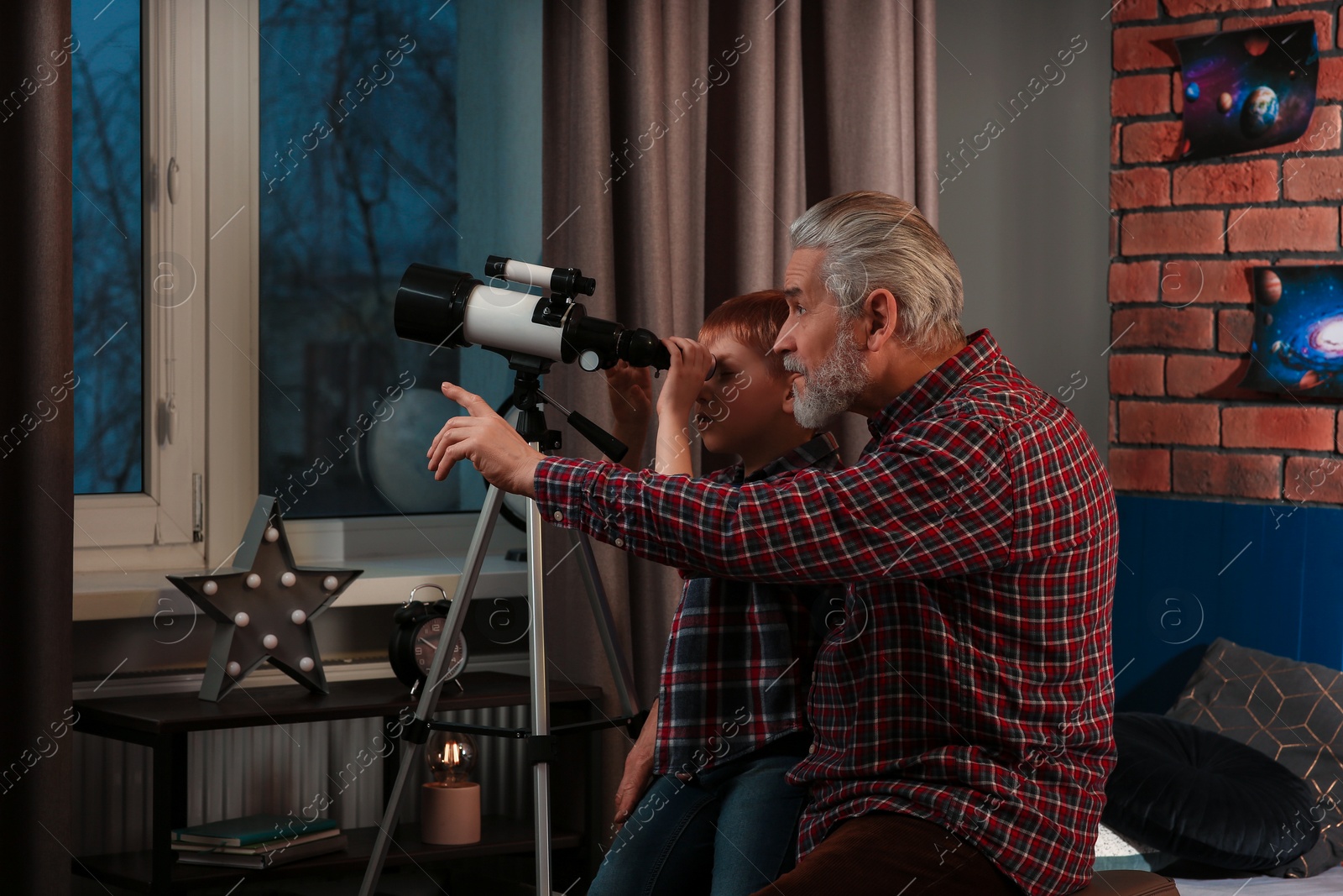 Photo of Little boy with his grandfather looking at stars through telescope in room