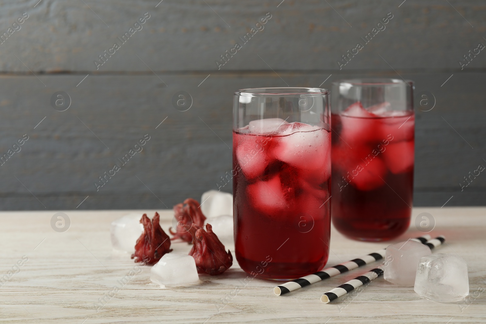 Photo of Delicious hibiscus tea with ice cubes, dry flowers and straws on white wooden table, space for text