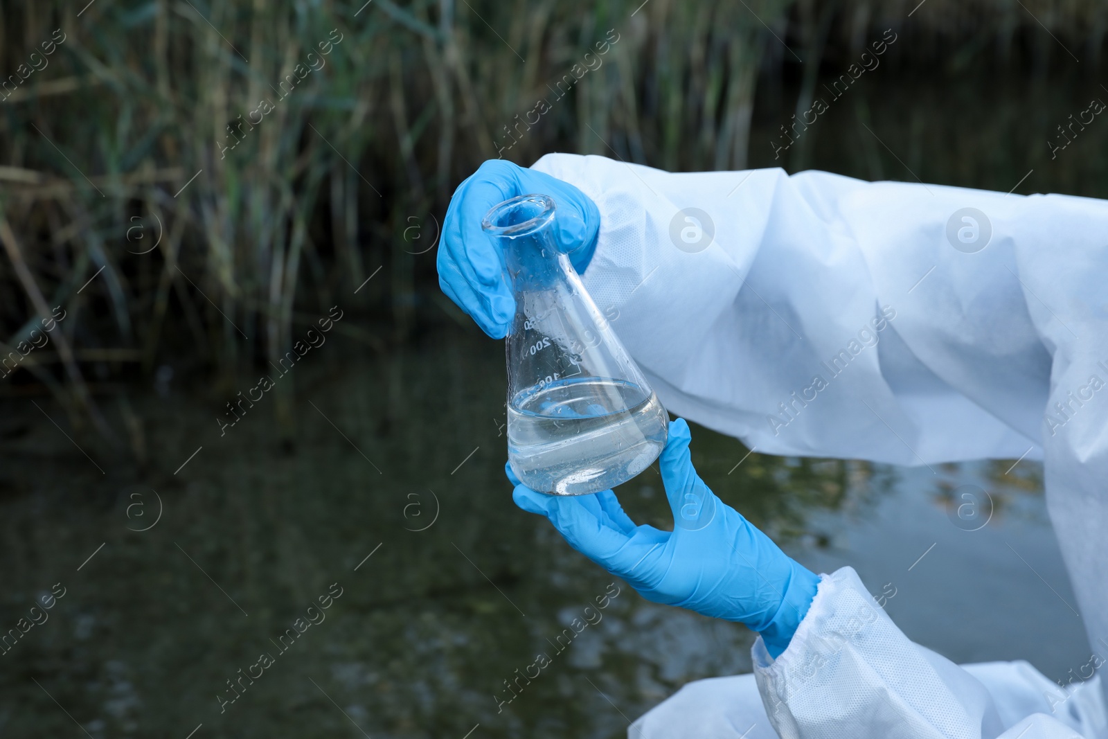 Photo of Scientist with conical flask taking sample from river for analysis, closeup