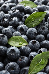 Photo of Wet fresh blueberries with green leaves as background, closeup
