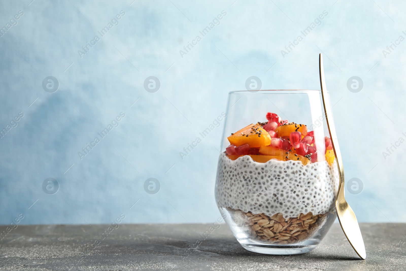 Photo of Glass of tasty chia seed pudding with granola, persimmon and pomegranate on table, space for text