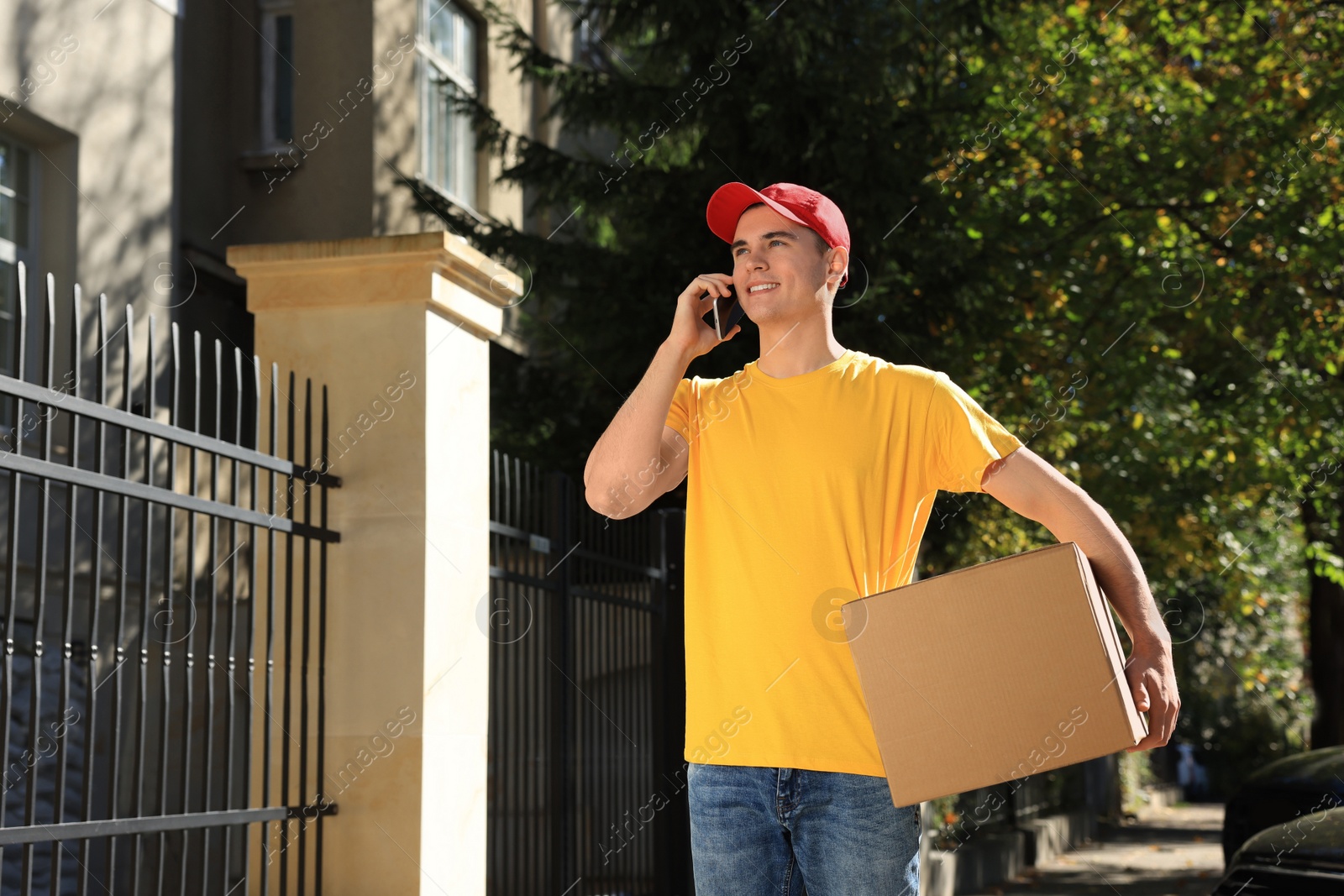 Photo of Courier with parcel talking by smartphone on city street