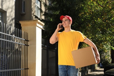 Photo of Courier with parcel talking by smartphone on city street