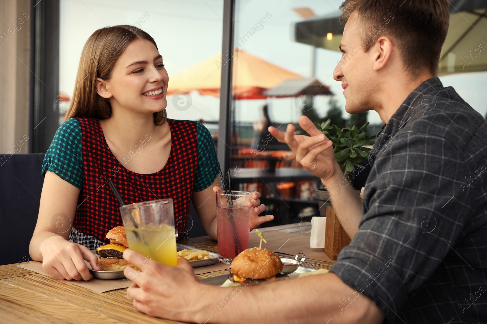 Photo of Young happy couple with burgers in street cafe