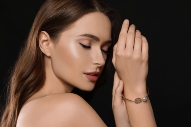 Young woman wearing elegant pearl bracelet on black background