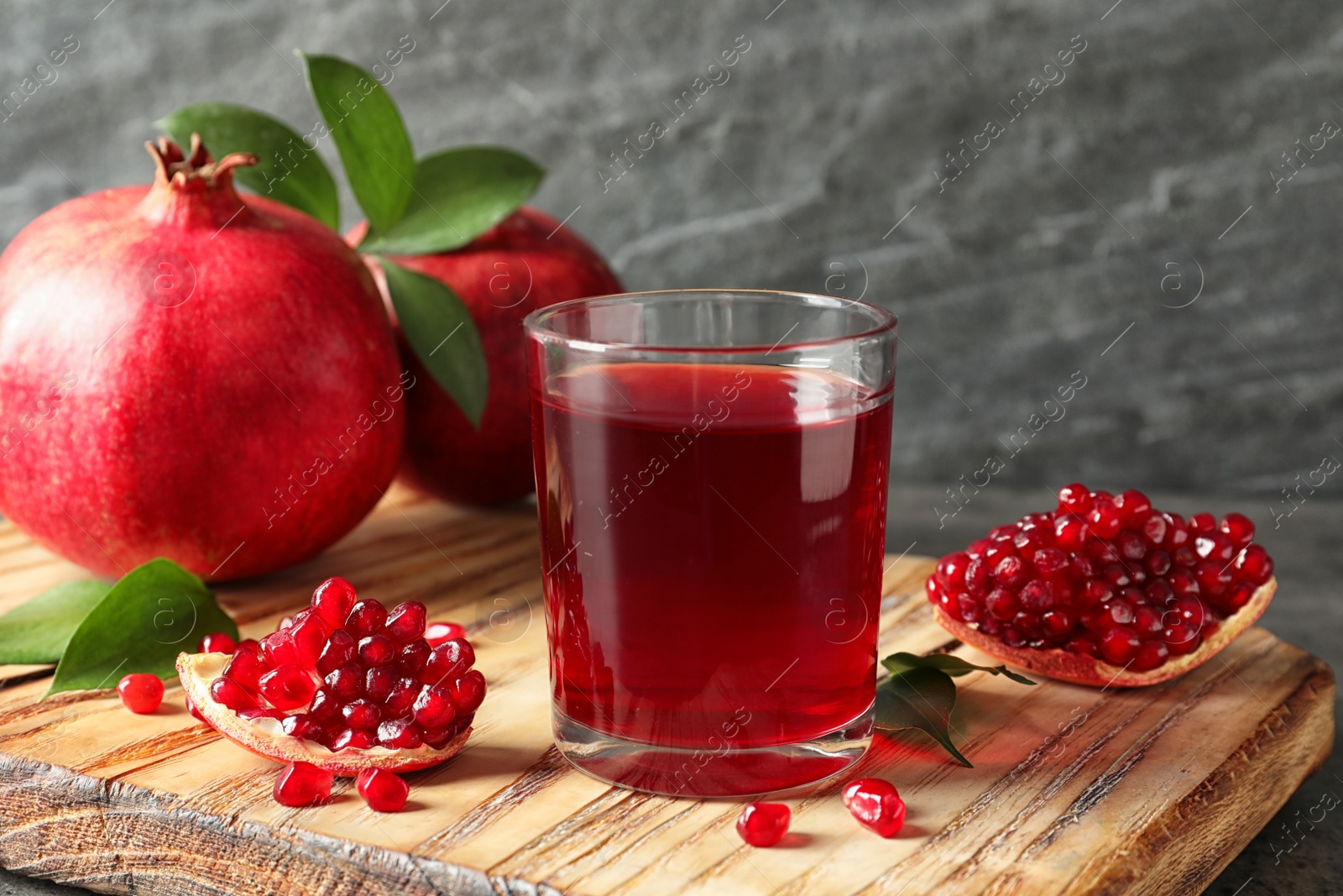 Photo of Glass of pomegranate juice and fresh fruits on wooden board against grey background