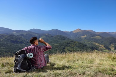 Photo of Tourist with hiking equipment looking through binoculars in mountains, back view