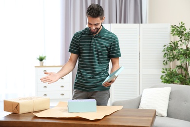 Photo of Young man opening parcel on table at home