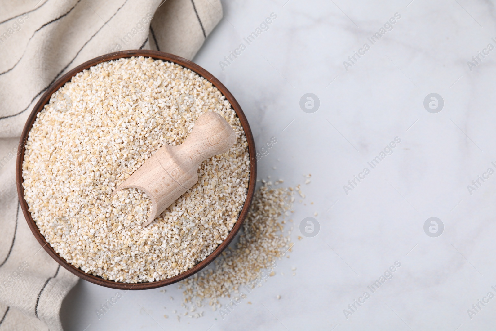 Photo of Dry barley groats and scoop in bowl on white table, top view. Space for text