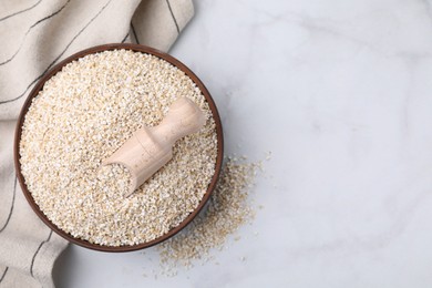 Dry barley groats and scoop in bowl on white table, top view. Space for text