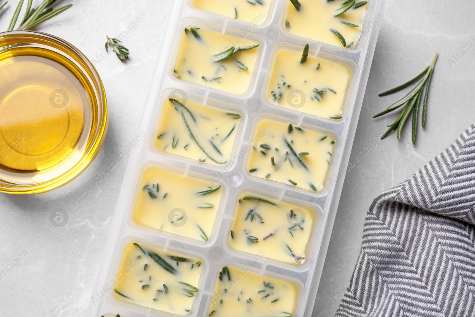 Photo of Ice cube tray with herbs frozen in oil and fresh rosemary on grey table, flat lay