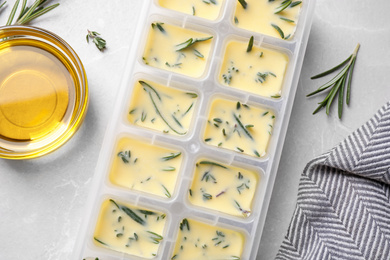 Photo of Ice cube tray with herbs frozen in oil and fresh rosemary on grey table, flat lay