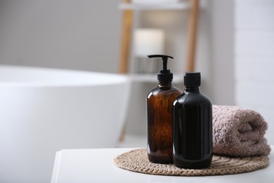 Photo of Bottles of bubble bath and towel on white table in bathroom, space for text