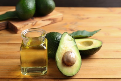 Photo of Jar of natural oil and avocados on wooden background