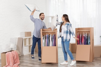 Photo of Young couple having pillow fight near wardrobe boxes at home