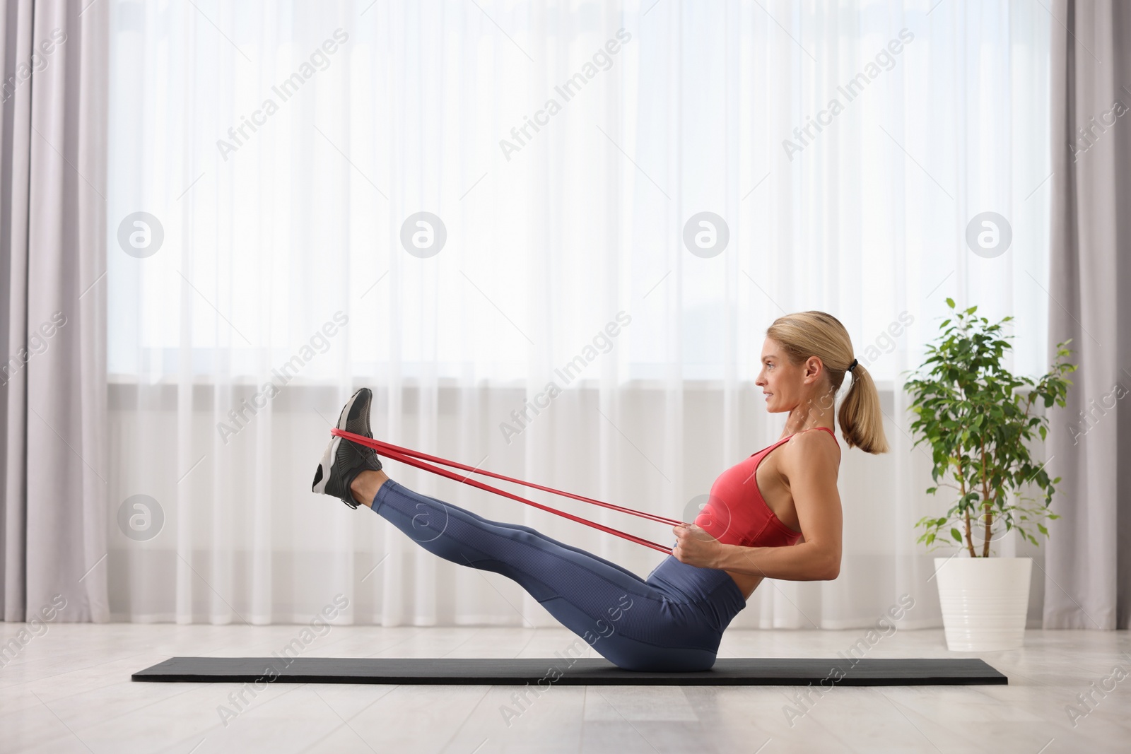 Photo of Athletic woman doing exercise with fitness elastic band on mat at home