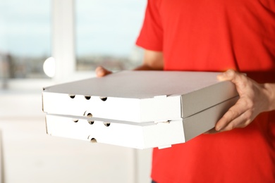 Photo of Young man with pizza boxes indoors, closeup. Food delivery service