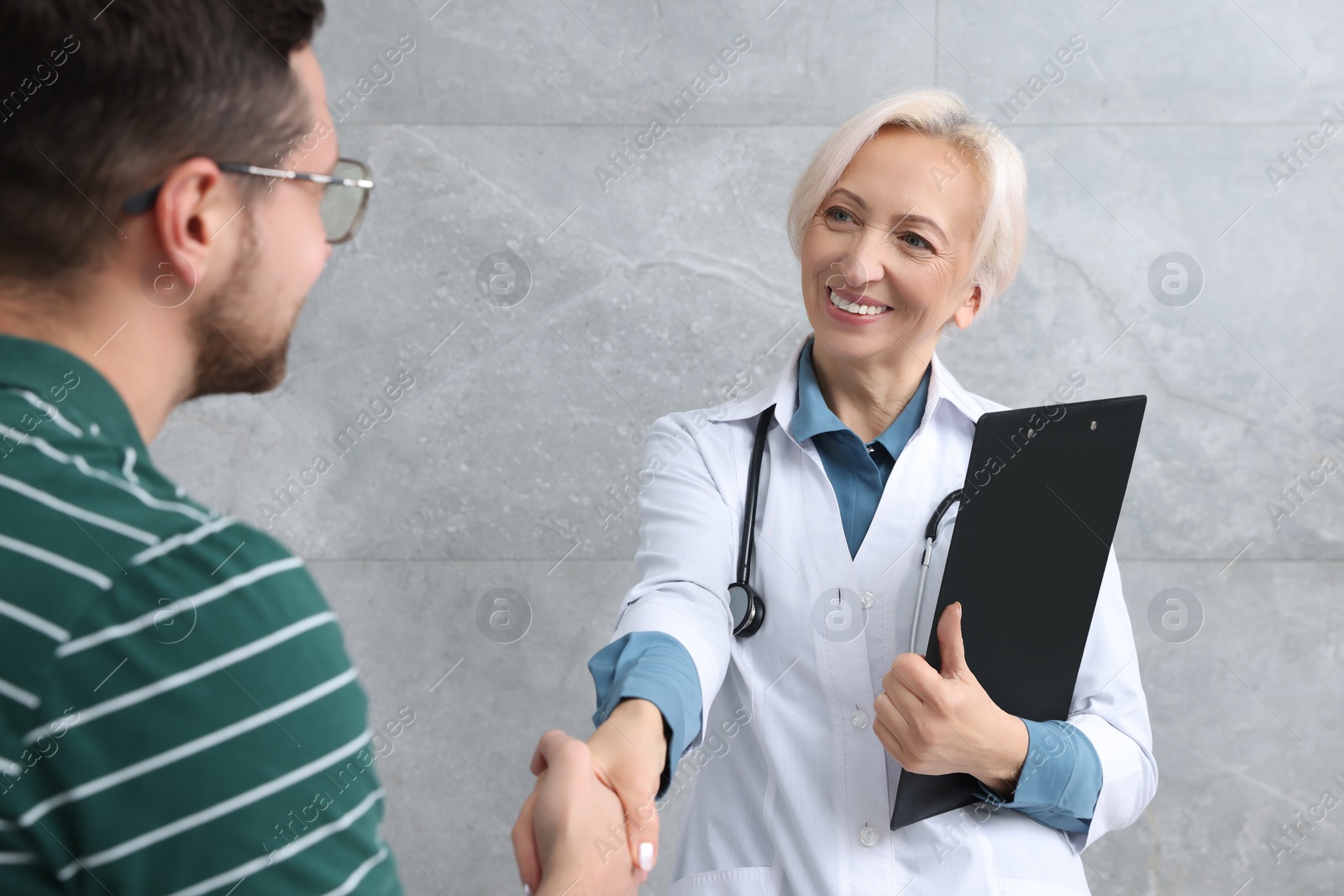 Photo of Doctor shaking hands with patient after consultation near grey wall