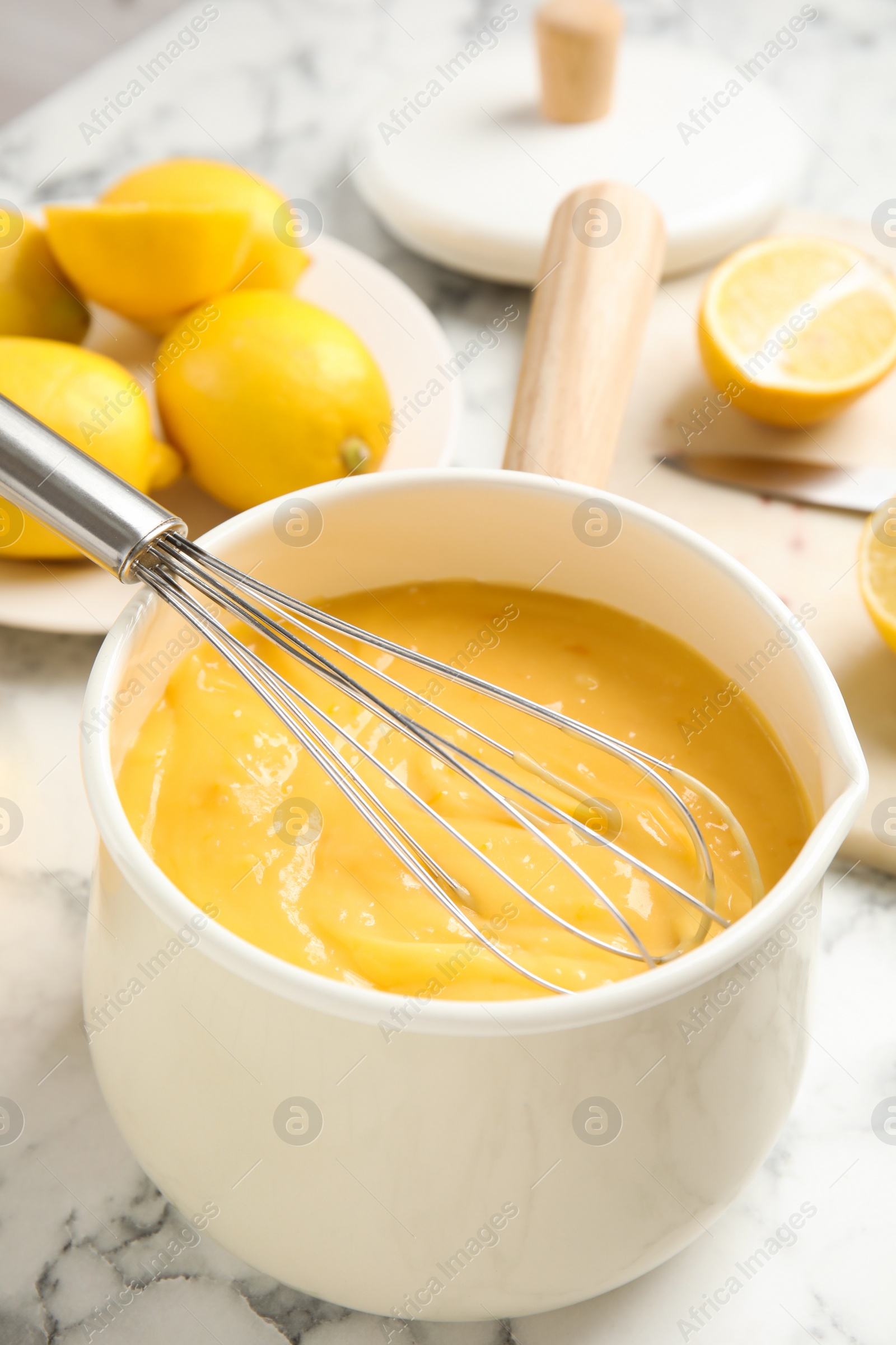 Photo of Delicious lemon curd and whisk on white marble table