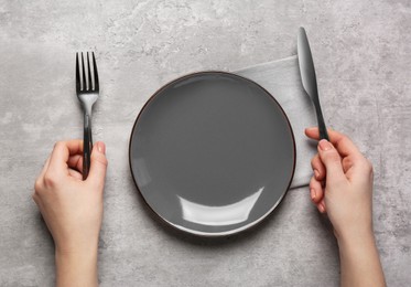 Photo of Woman with empty plate and cutlery at light grey table, top view