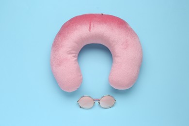 Photo of Pink travel pillow and sunglasses on light blue background, flat lay