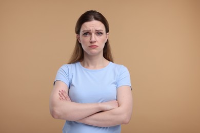 Photo of Portrait of sad woman with crossed arms on beige background