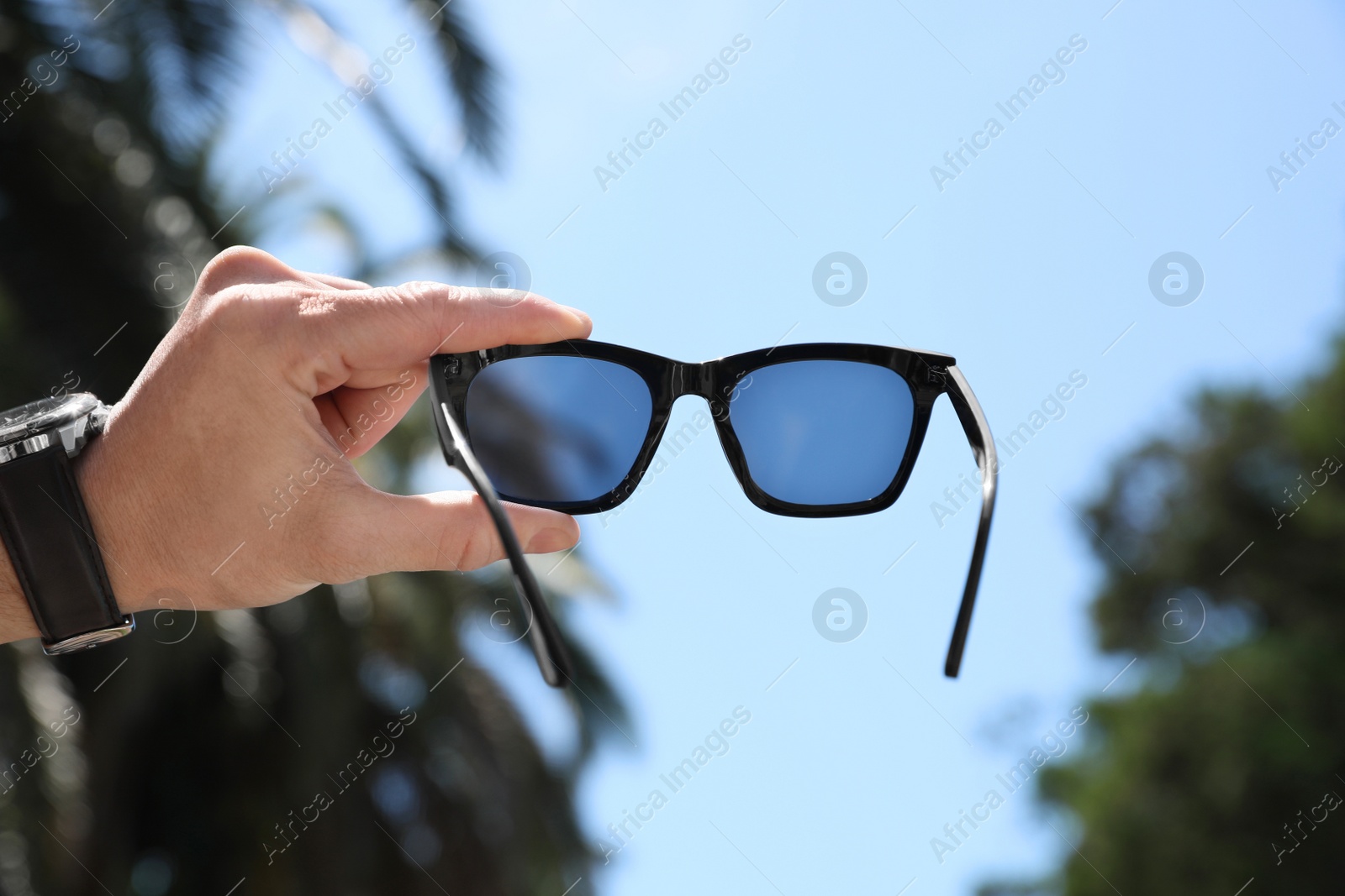 Photo of Mature man holding stylish sunglasses outdoors on sunny day, closeup