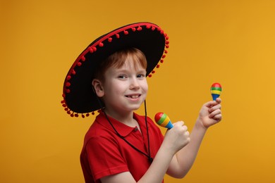 Photo of Cute boy in Mexican sombrero hat with maracas on yellow background