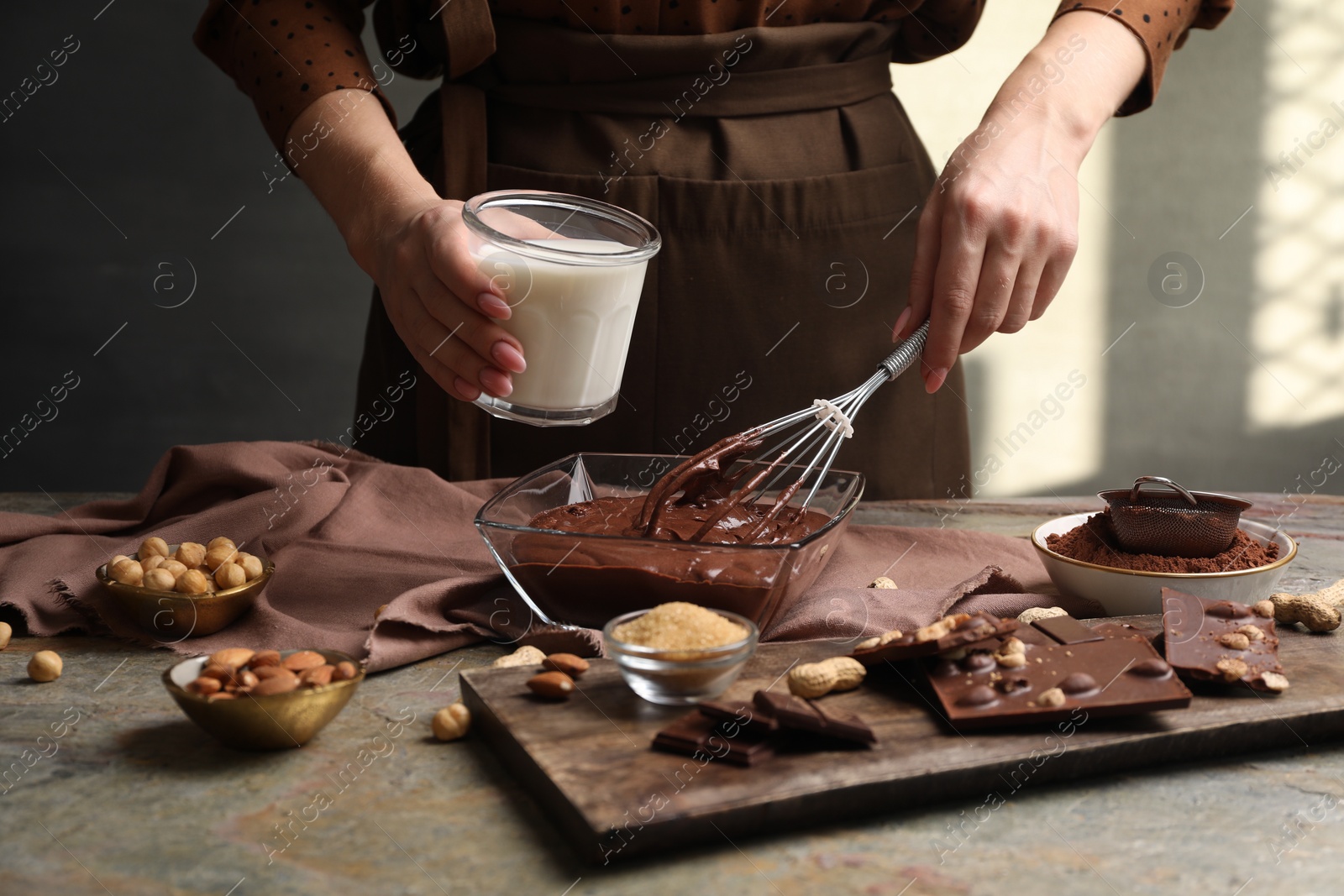 Photo of Woman with glass of milk and whisk mixing delicious chocolate cream at textured table, closeup