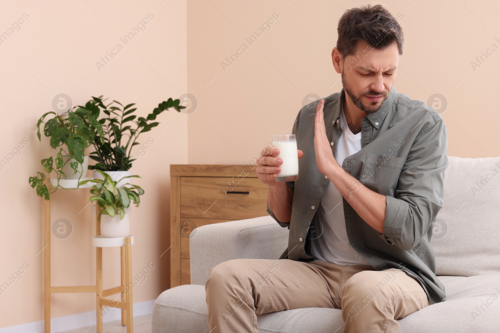 Photo of Man with glass of milk suffering from lactose intolerance at home, space for text