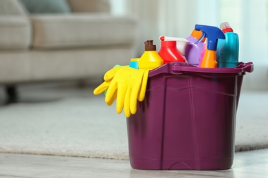 Photo of Plastic bucket with different cleaning products on floor indoors, space for text